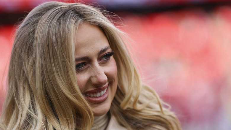 Brittany Mahomes covering her face with white and rose-printed handbag