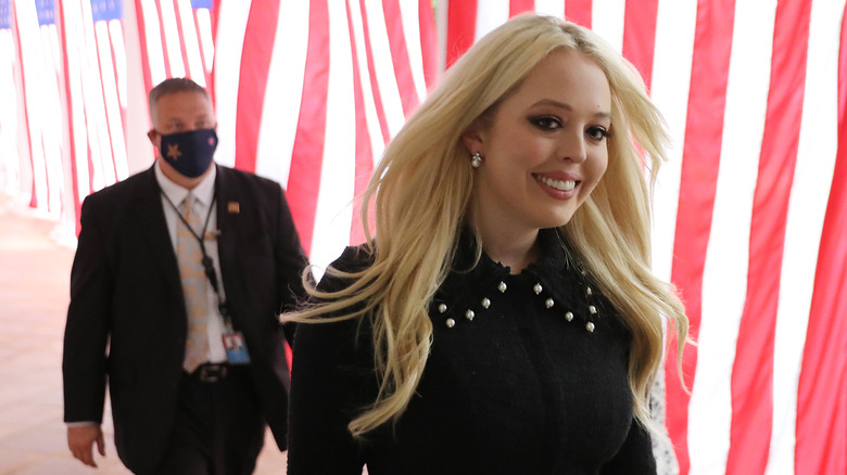 Tiffany Trump walking while smiling in a black outfit next to American flags