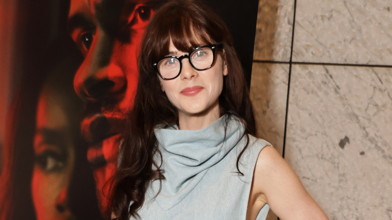 Zooey Deschanel wearing glasses and smiling on the red carpet of a movie premiere