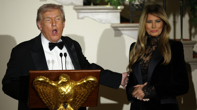 Donald Trump opens his mouth wide to speak and touches Melania Trump's arm as she smiles beside him at the 2025 Congressional Ball.