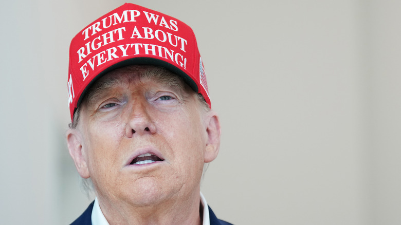 A pale-skinned Donald Trump wears a red "Trump was right about everything" hat during a visit to The People's House museum.