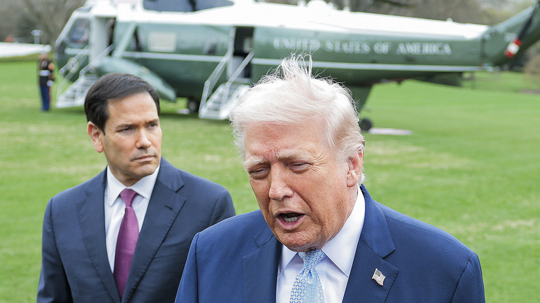 As his hair lifts up, Donald Trump speaks with Marco Rubio standing behind him and Marine One in the background.