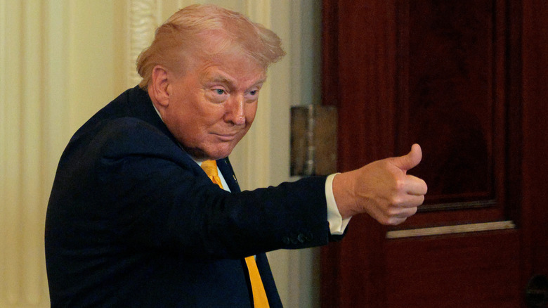Donald Trump smiles, ducks his head down, extends his arm out, and gives a thumbs-up.