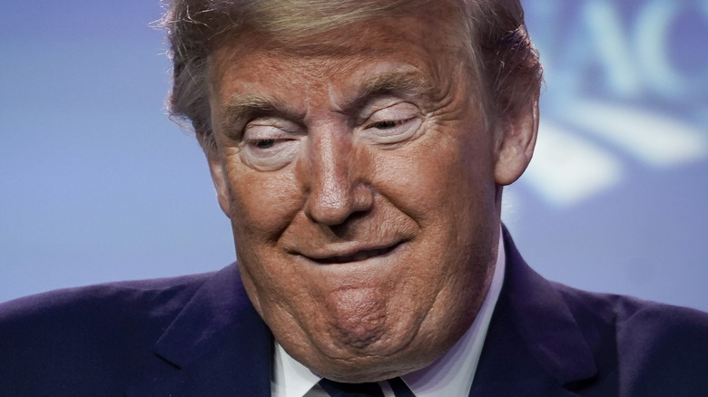 Donald Trump bites his lower lip and looks down.