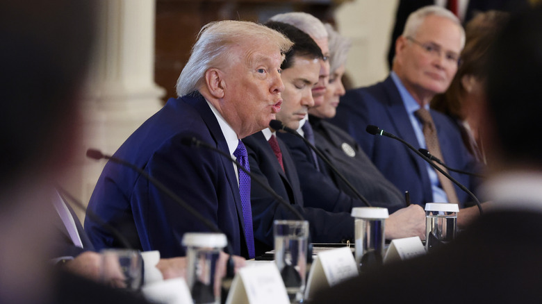 A seated Donald Trump sticks his lips out as he speaks beside Marco Rubio during a meeting.