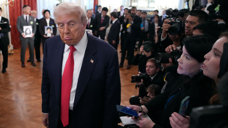 Donald Trump sticks his bottom lip out as he walks past the media gathered inside Tokyo's Akasaka Palace.