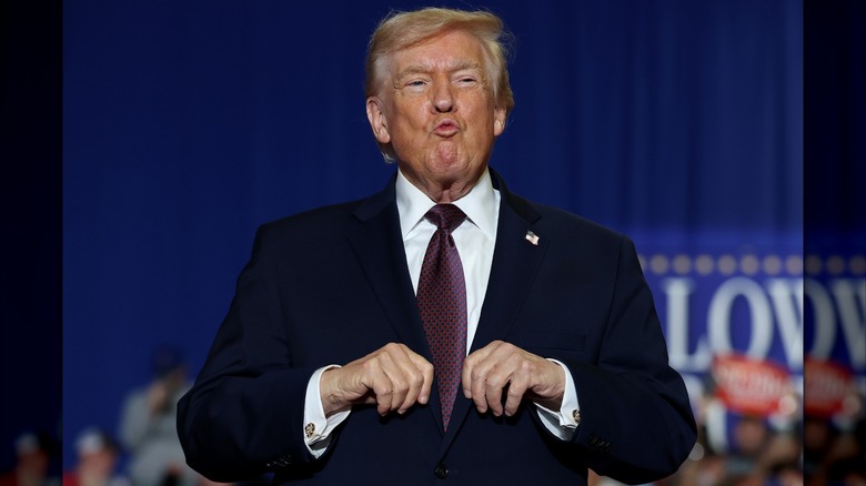 Donald Trump holds his hands in front of his chest and makes a kissy face.