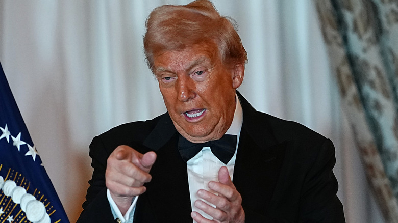 A sweaty Donald Trump wears a tuxedo and points while opening his mouth to speak.