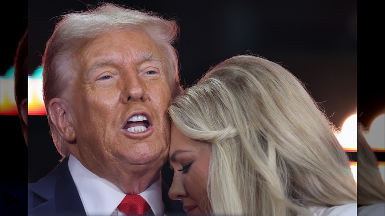 Erika Kirk rests her forehead on Donald Trump's cheek as he opens his mouth to speak.