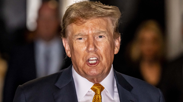 A sweaty Donald Trump frowns while opening his mouth to speak.