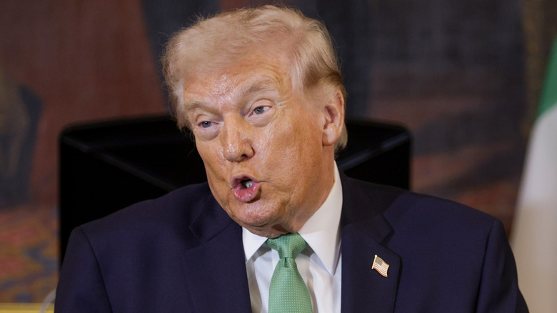A sweaty-faced Donald Trump wears a green tie and makes an "O" with his mouth while speaking.