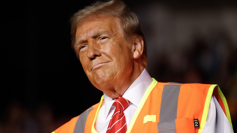 Donald Trump smiles while wearing an orange safety vest and red and white striped tie.
