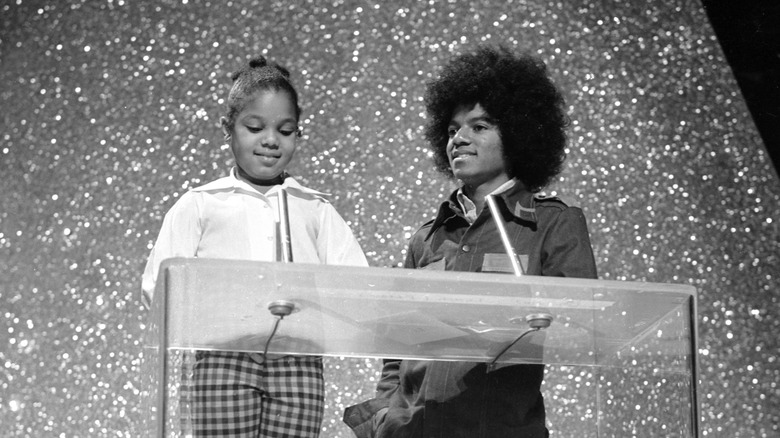 Young Janet Jackson standing at a podium next to a smiling teenage Michael Jackson.