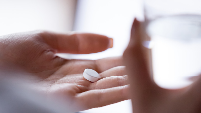 hand holding a glass and a pill