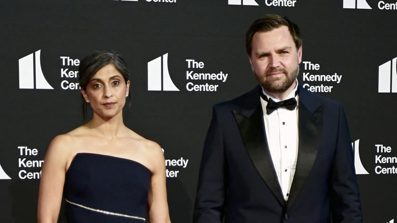 Usha Vance posing with neutral expression in a black strapless dress next to JD Vance in a tuxedo