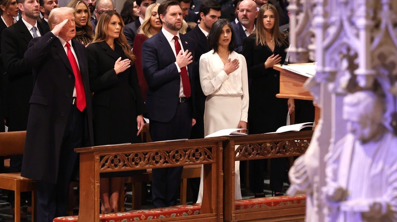 Usha Vance wearing a white shirt and skirt with her hand on her chest while at the National Prayer Service at Washington National Cathedral.
