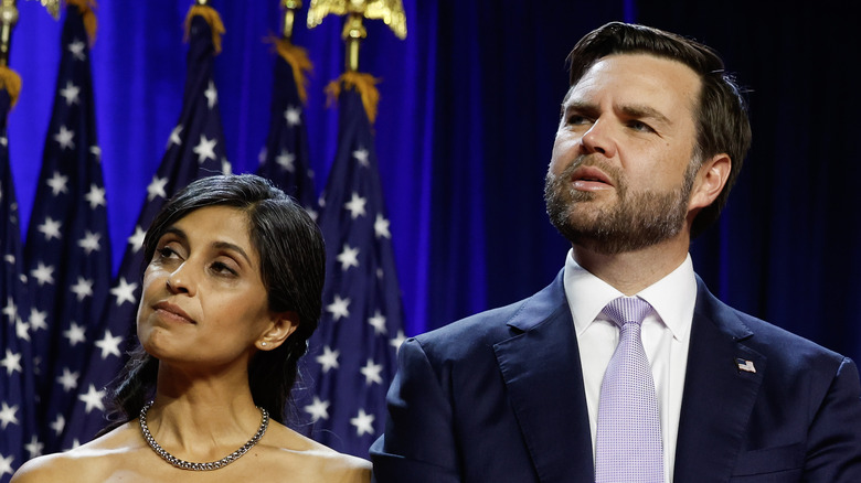 JD Vance wearing a suit and purple tie next to Usha Vance, wearing a black dress, as they stand on stage at the Palm Beach convention center.