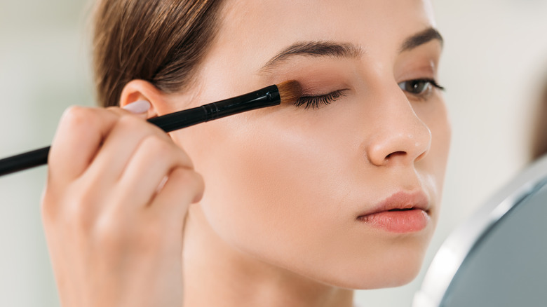 woman applying makeup to eyelid with brush