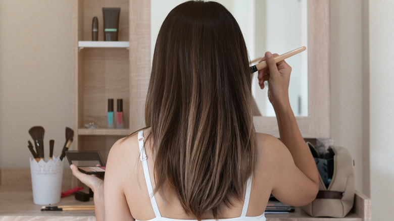 Woman applying makeup at vanity 