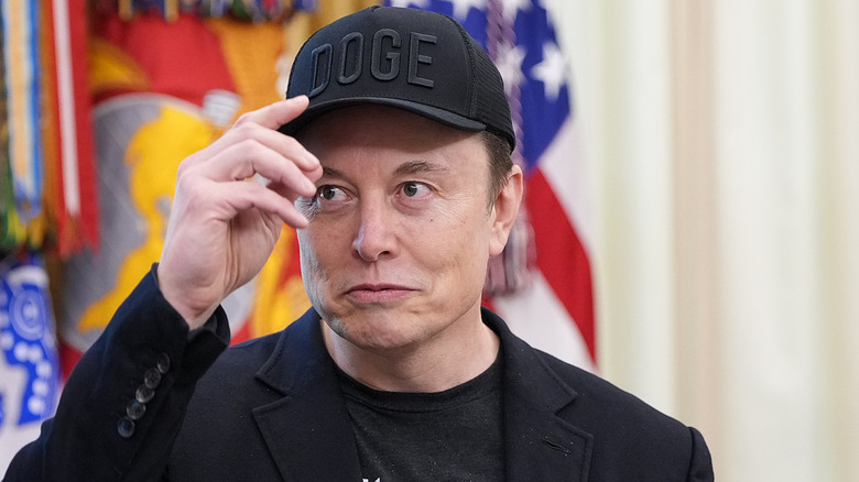 Elon Musk wearing a black Doge hat.