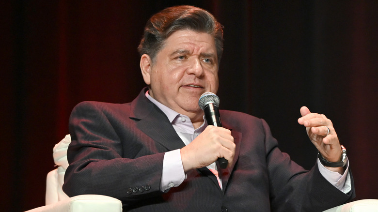J.B. Pritzker speaking into a microphone in a black suit