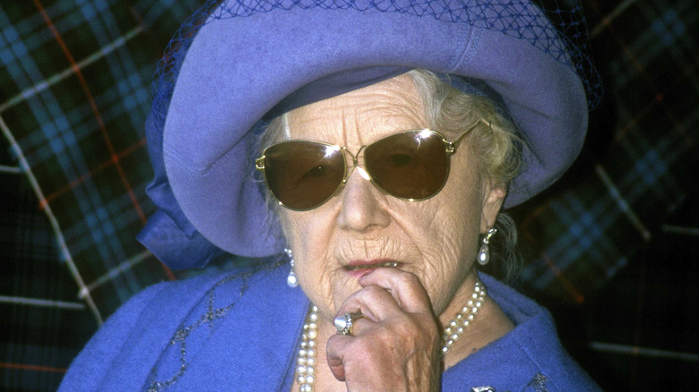 The Queen Mother, wearing sunglasses and a fancy hat, while looking deep in thought