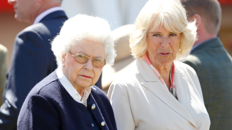 Queen Camilla speaking to a serious-looking Queen Elizabeth II