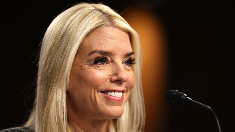 Pam Bondi smiles in front of a microphone