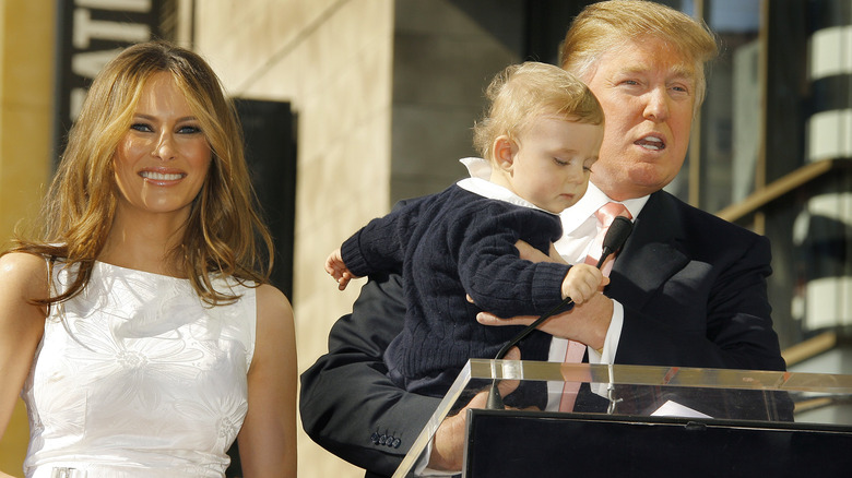 Donald Trump holding a smiling baby Barron Trump with a smiling Melania Trump next to him