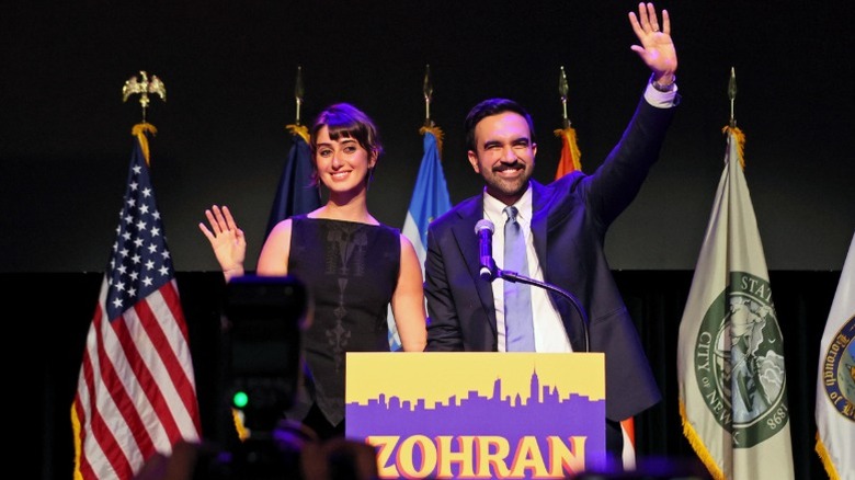Rama Duwaji and Zohran Mamdani wave behind a podium in Brooklyn, New York City, NY (2025)