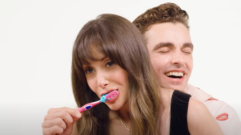 Dave Franco standing behind Alison Brie and brushing her teeth