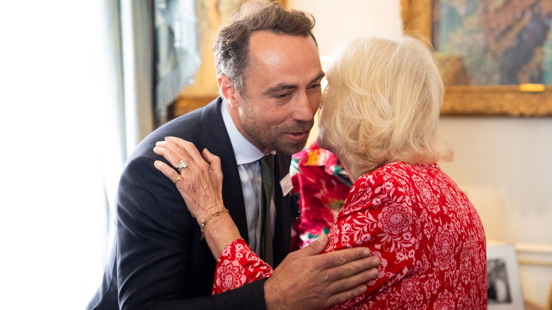 James Middleton and Queen Camilla kissing each other on the cheek at an event at Clarence House