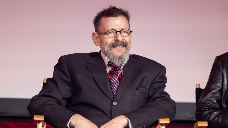 Judd Nelson on stage wearing glasses and smiling.