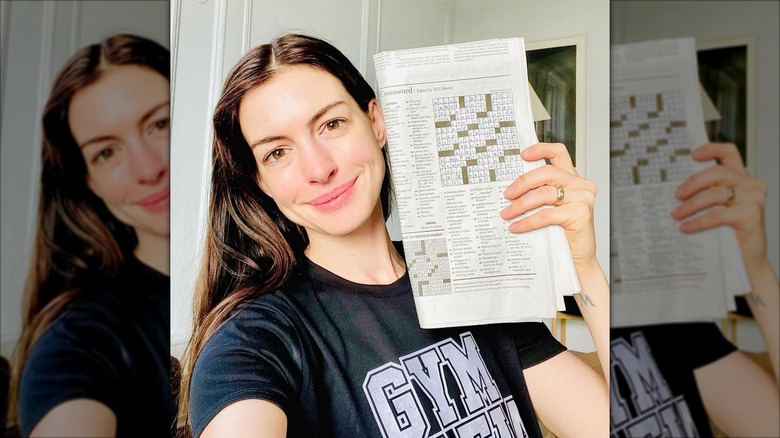 Anne Hathaway smiles as she holds up a New York Times newspaper (2021)
