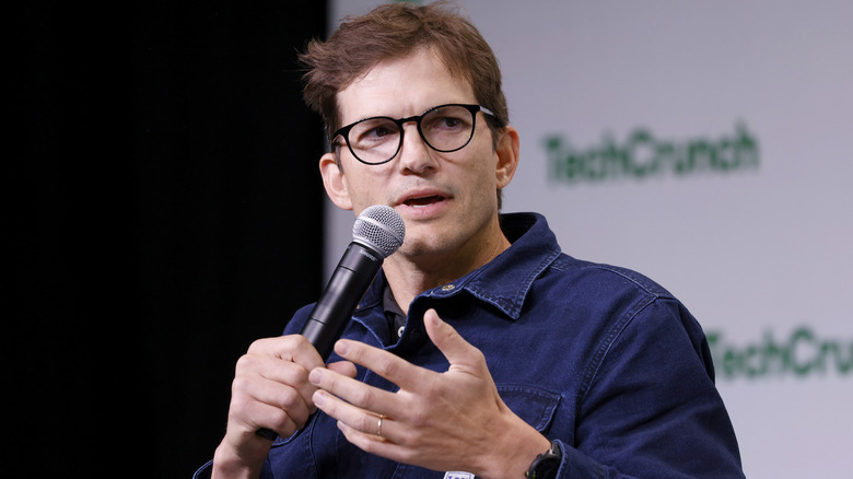 Ashton Kutcher speaking into mic onstage during TechCrunch