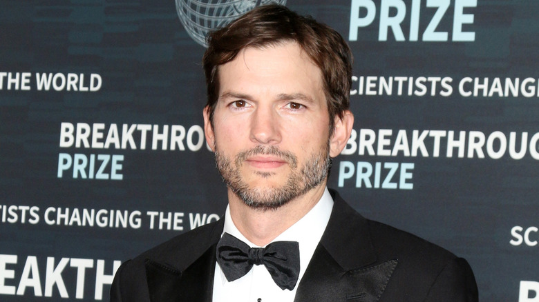 Ashton Kutcher posing on step-and-repeat in tux
