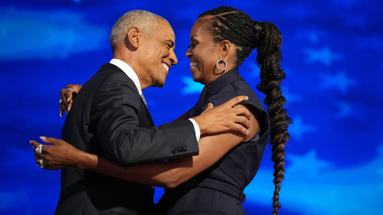 Barack and Michelle Obama hugging onstage in front of a blue background