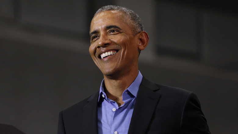 Barack Obama smiling while posing in front of a dark background