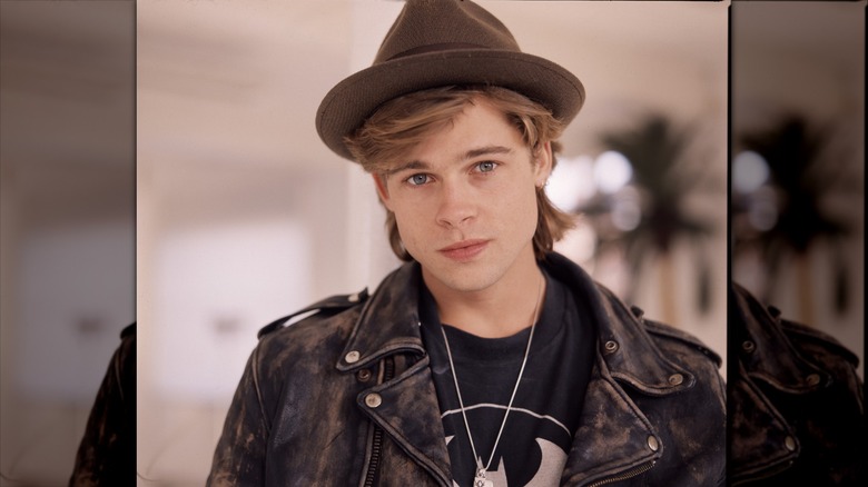 Brad Pitt early in his career wearing a brown fedora and leather jacket.