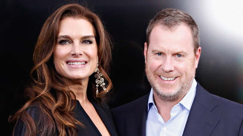Brooke Shields and husband Chris Henchy smile for a photo against a black backdrop