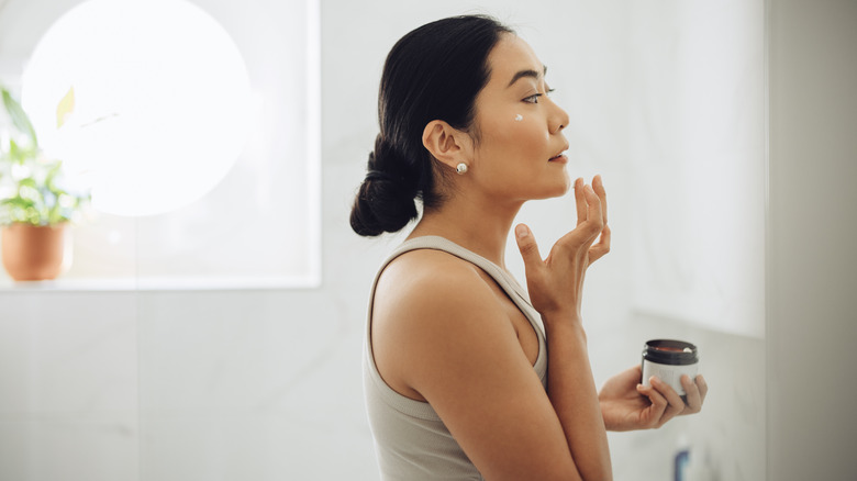 Woman holding facial moisturizer with product on face