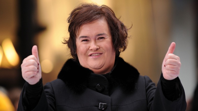 Susan Boyle in a winter coat giving two thumbs up