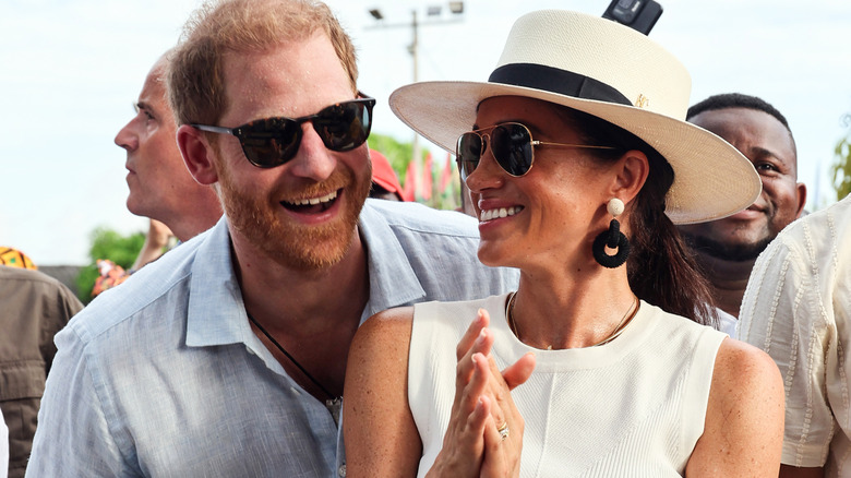 Prince Harry and Meghan Markle sharing a laugh while wearing sunglasses