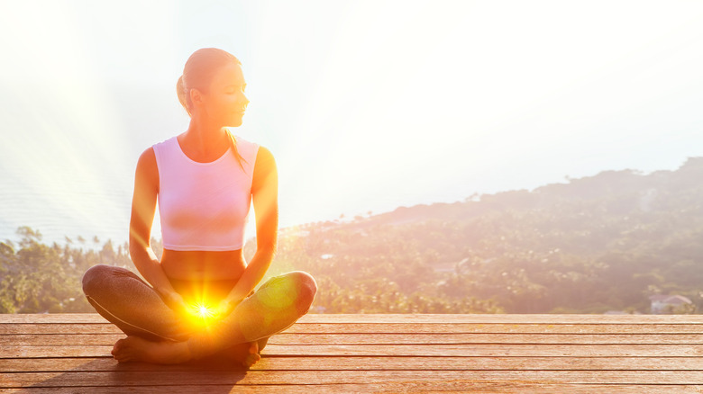 A woman sitting in lotus position with her sacral chakra lit up 