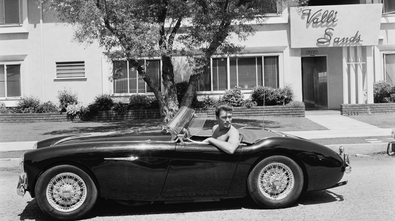 Clint Eastwood at the wheel of Austin Healey 100M sports car outside his home in Los Angeles, California, 1st June 1956. The building in the background has a sign above the entrance reading 'Valli Sands'.
