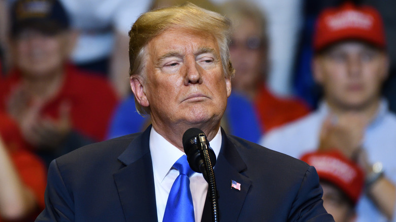 Donald Trump standing at microphone at rally with serious expression
