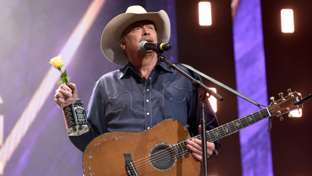 Alan Jackson holds a Jack Daniels bottle and his guitar.