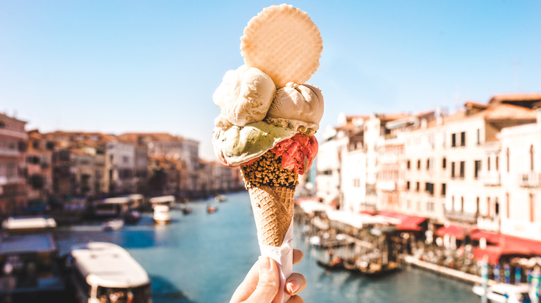 Different flavors of ice cream in a waffle cone in front of a waterfront city