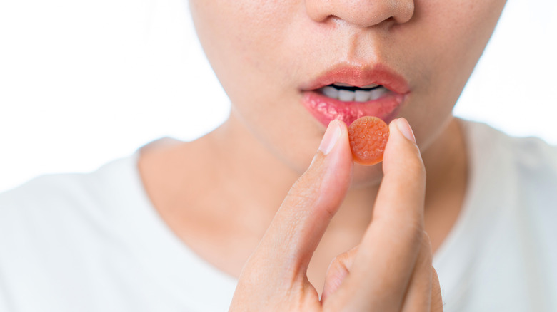 Woman holding melatonin gummy in front of her mouth.