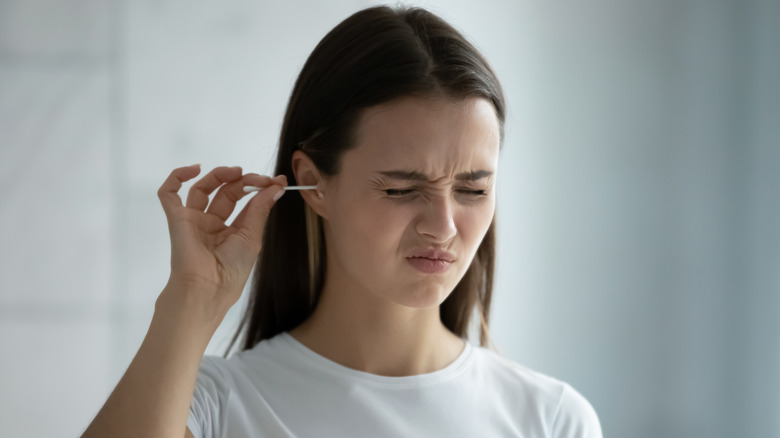 Young woman cleaning her ear and wincing in pain